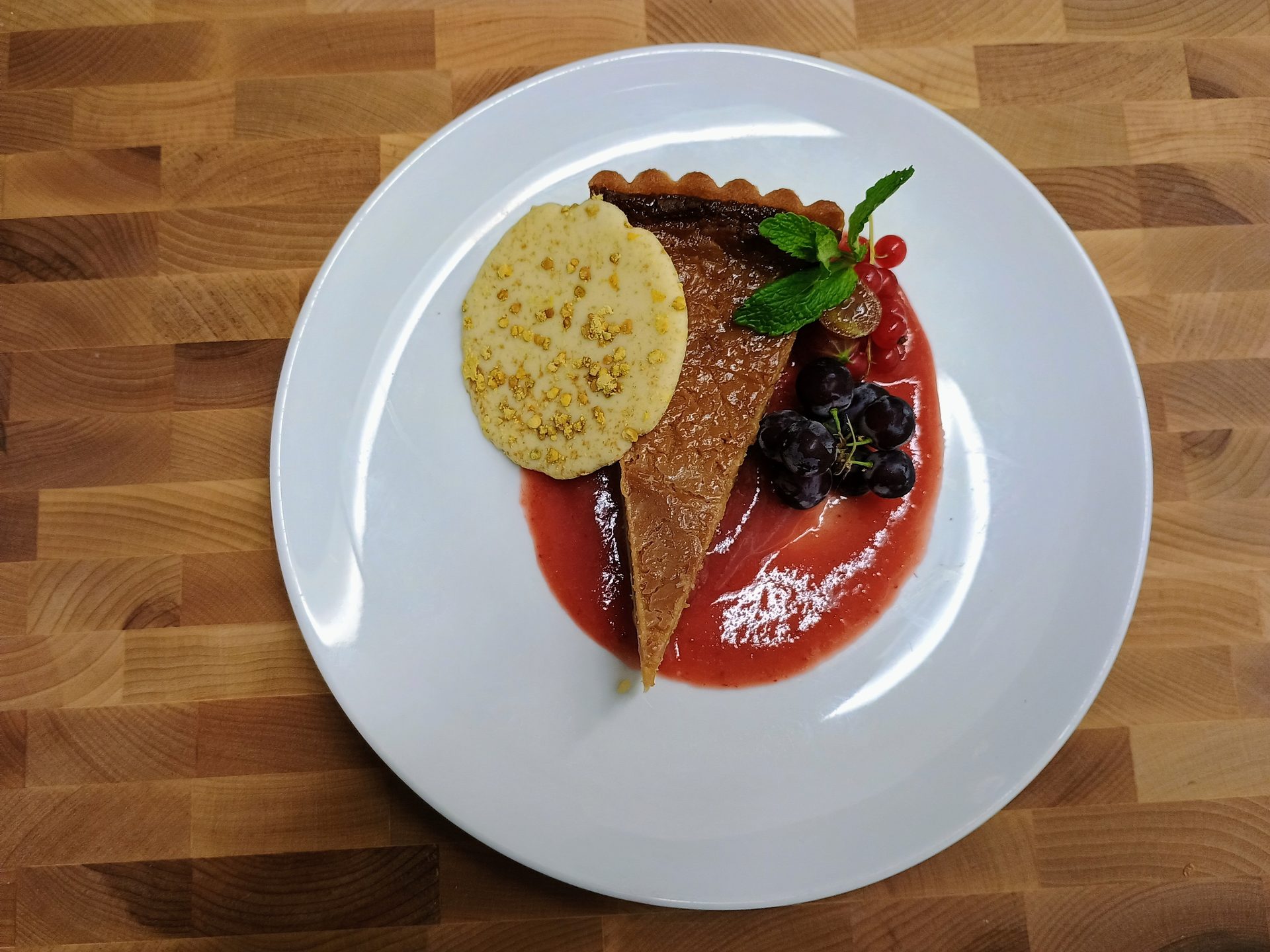 A slice of tart with berry coulis and a shortbread biscuit